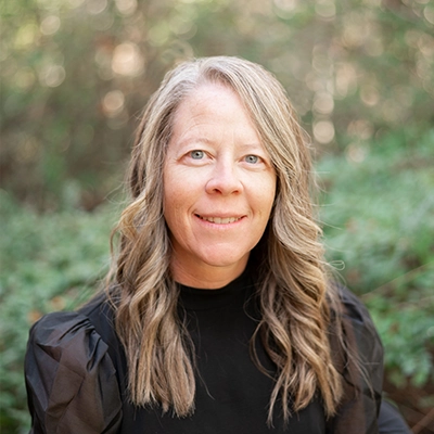 Carrie Watkins smiling outside, with greenery in the background.