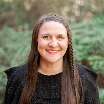 Casey Santangelo smiling outside, with greenery in the background.