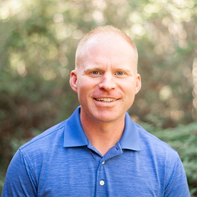 Matthew Liles smiling outside, with greenery in the background.